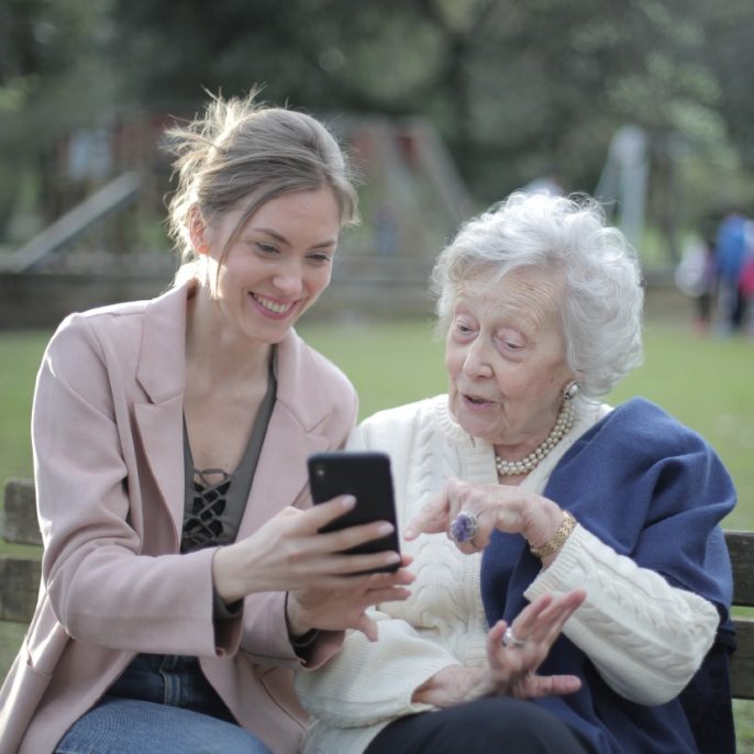 idős és fiatal nő mobiltelefont néz a parkban