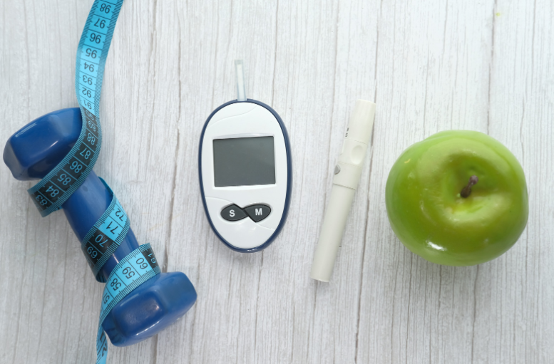 egy kézi súlyzó, egy vércukormérő és egy zöld alma