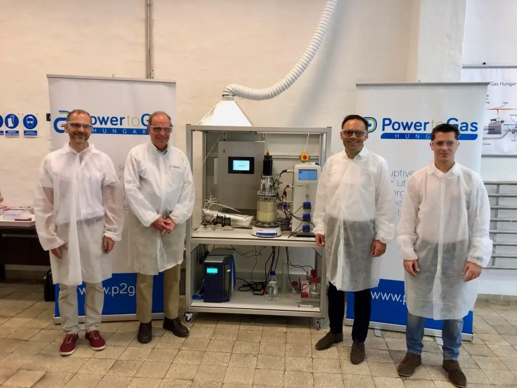 A Power-to-Gas Hungary Kft által fejlesztett biometanizációs prototípus a startup oroszlányi laboratóriumában. Balról jobbra: Dr. Sinóros-Szabó Botond műszaki igazgató, Dr. Laurens J. Mets professzor, a power-to-gas technológia szabadalmaztatója, Dr. Csedő Zoltán ügyvezető igazgató, Zavarkó Máté üzletfejlesztési igazgató.