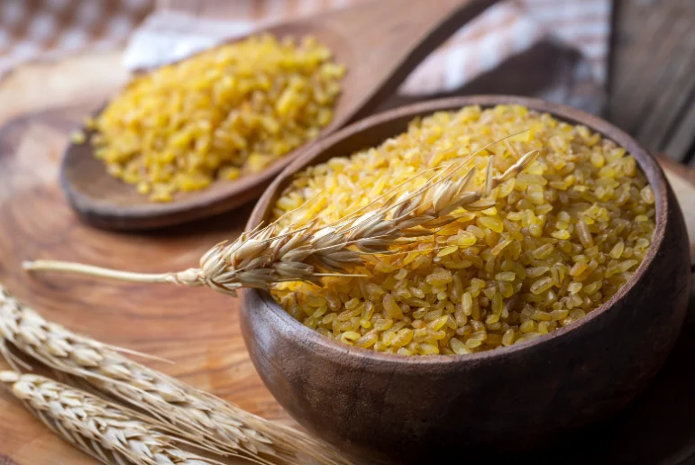egy tál bulgur, pár gabonaszál, a háttérben egy kanál bulgur 
